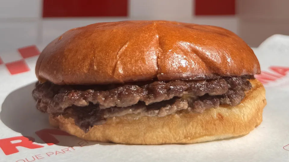 The 1976 de Woody's Factory vu de face : deux steaks smashés à la croûte dorée dans un potato bun, devant un carrelage rouge et blanc