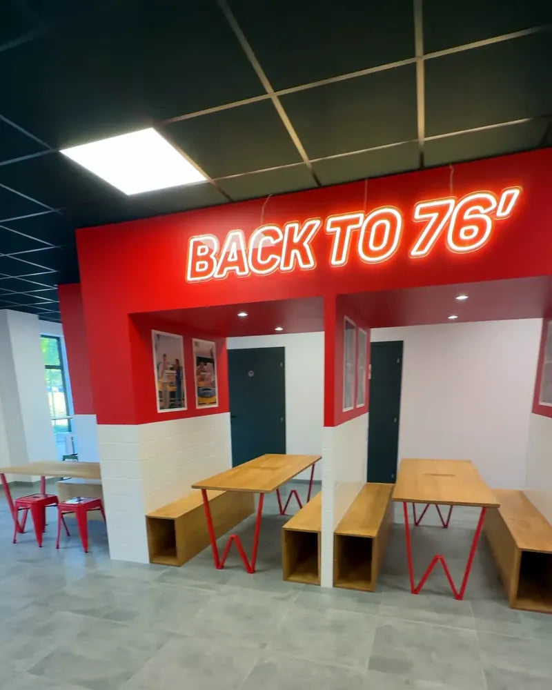 Alcôve Back to 76' de Woody's Factory Lens : murs rouges, néon et grandes tables en bois