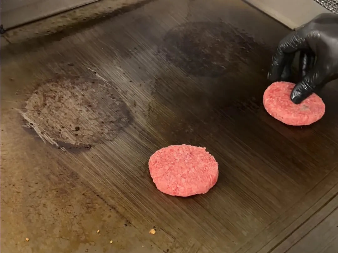 Deux boules de bœuf haché posées sur la plaque de cuisson, juste avant le smash