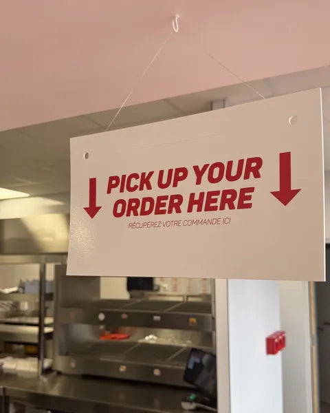 Panneau « Pick up your order here » au-dessus du comptoir de retrait des commandes de Woody's Factory Lens
