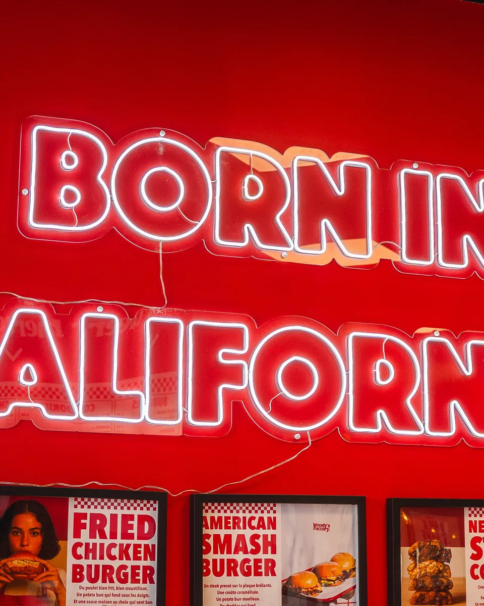 Néon Born in California sur le mur rouge de Woody's Factory Douai, au-dessus des affiches de burgers