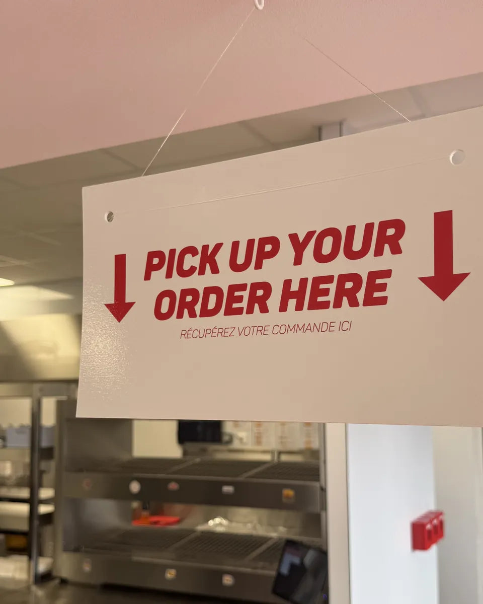 Panneau « Pick up your order here » au-dessus du comptoir de retrait des commandes de Woody's Factory Lens