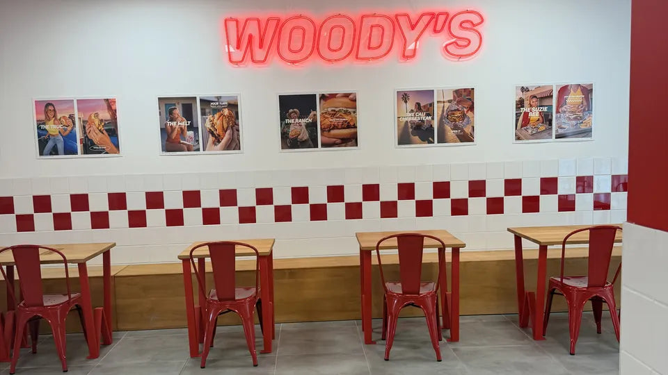 La salle de Woody's Factory Lens face au néon rouge WOODY'S, tables en bois et chaises rouges, à 4 minutes à pied du stade Bollaert-Delelis