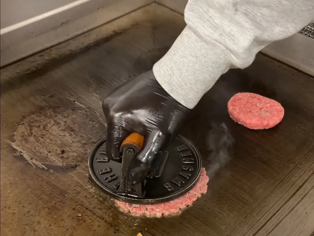 Un cuisinier ganté écrase une boule de bœuf au presse sur la plaque : le smash