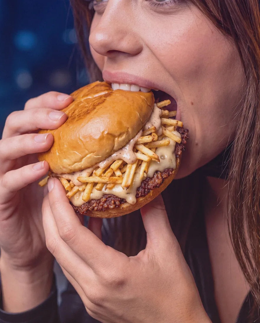 Une jeune femme croque dans The Nightmare, le smash burger d'Halloween de Woody's Factory, tenu à deux mains