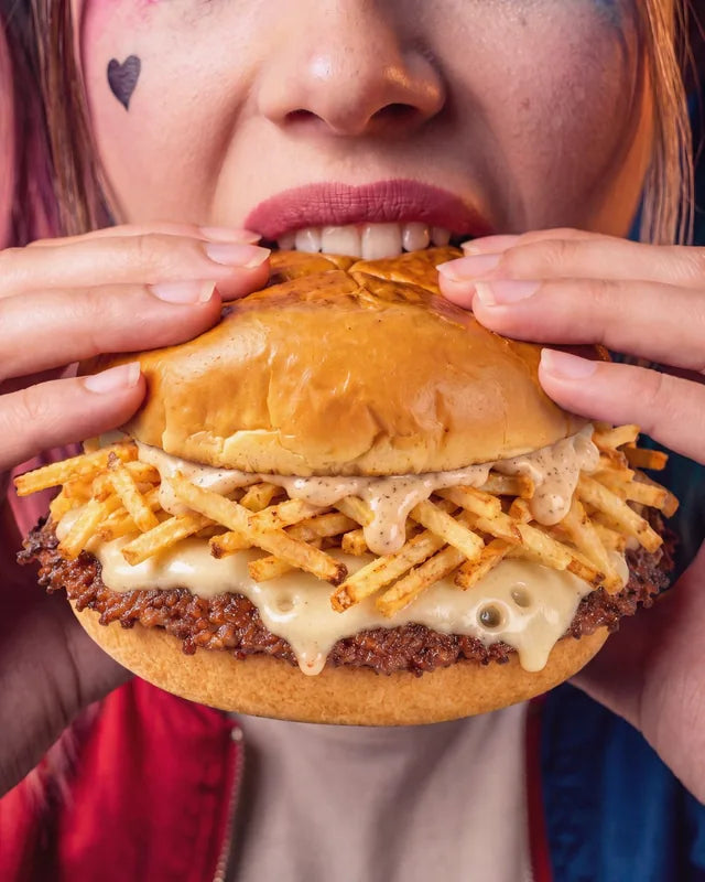 Gros plan sur The Nightmare croqué à pleines dents, le smash burger d'Halloween de Woody's Factory : chips fines en bâtonnets, sauce au poivre et emmental fondu
